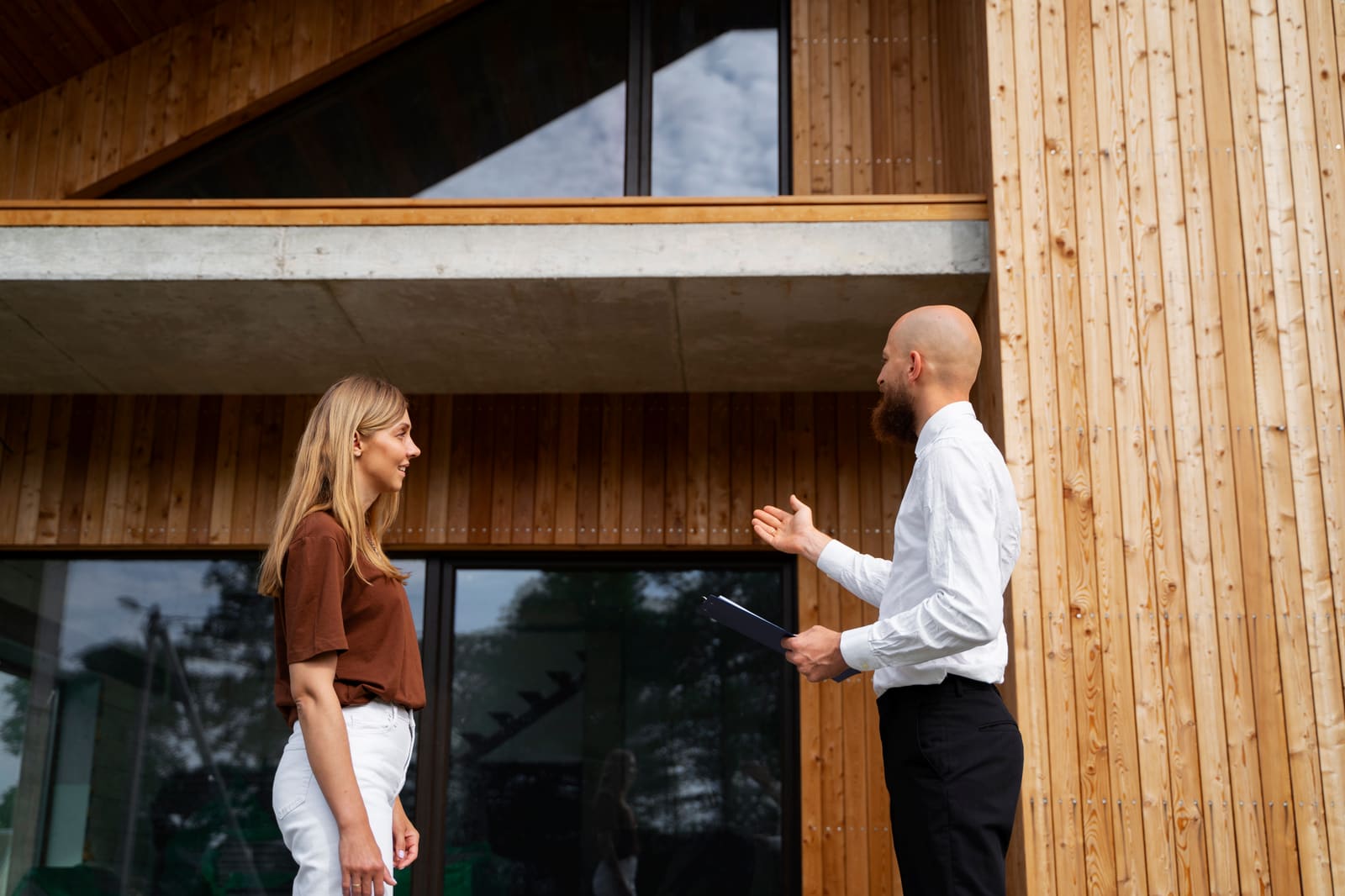 A homeowner talking with her agent outside a modern wood-clad house