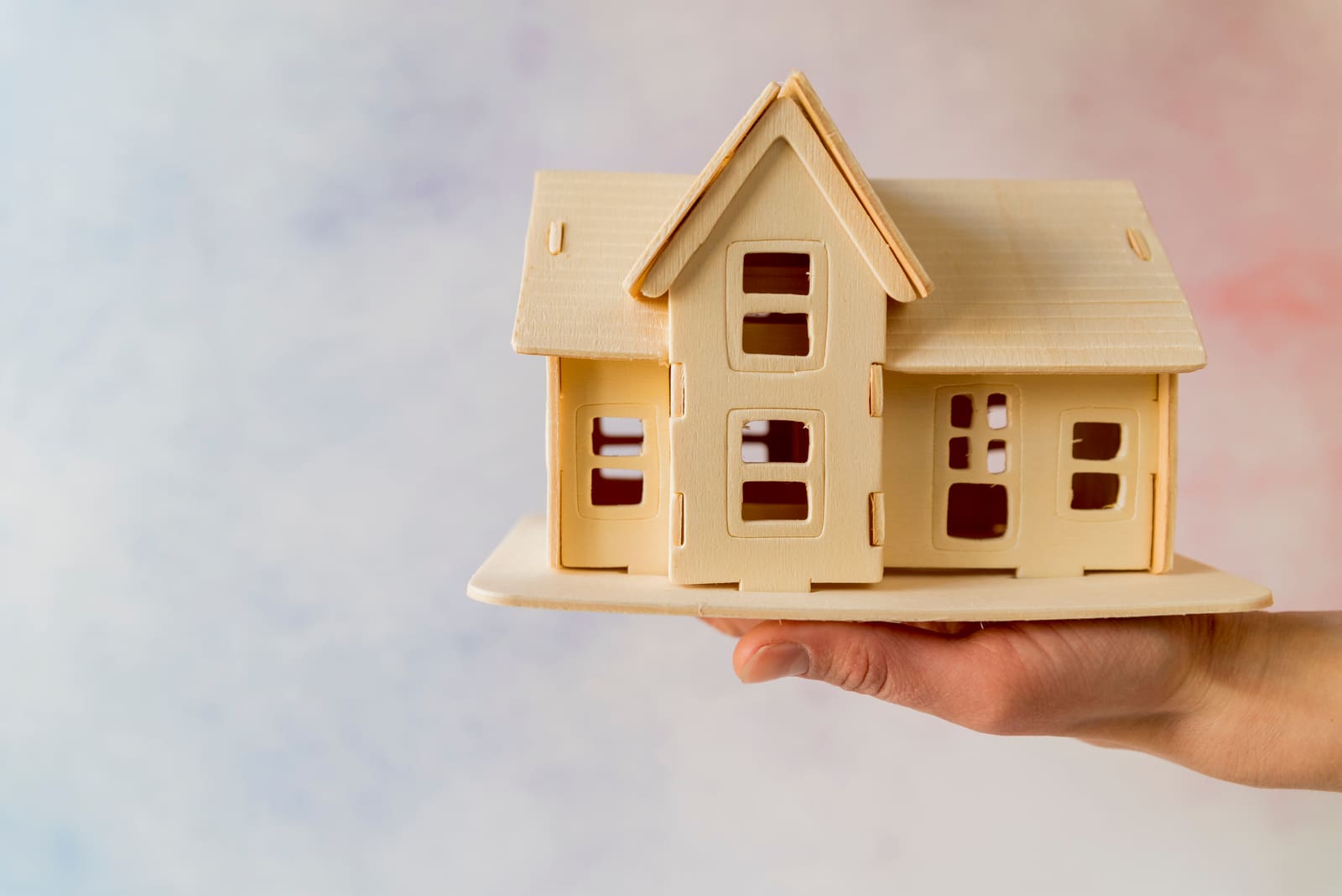 A hand holding a small wooden model of a house